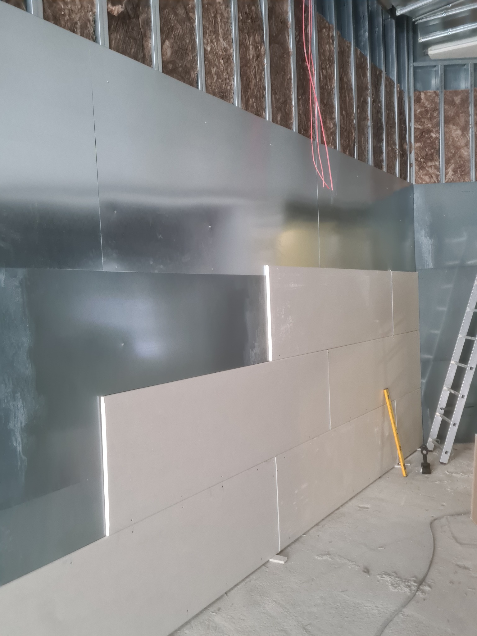 Montaż płyt karton-gips na metalowej konstrukcji. Widoczne ocieplenie wełną mineralną, poziomica i drabina. Etap prac wykończeniowych w pomieszczeniu.