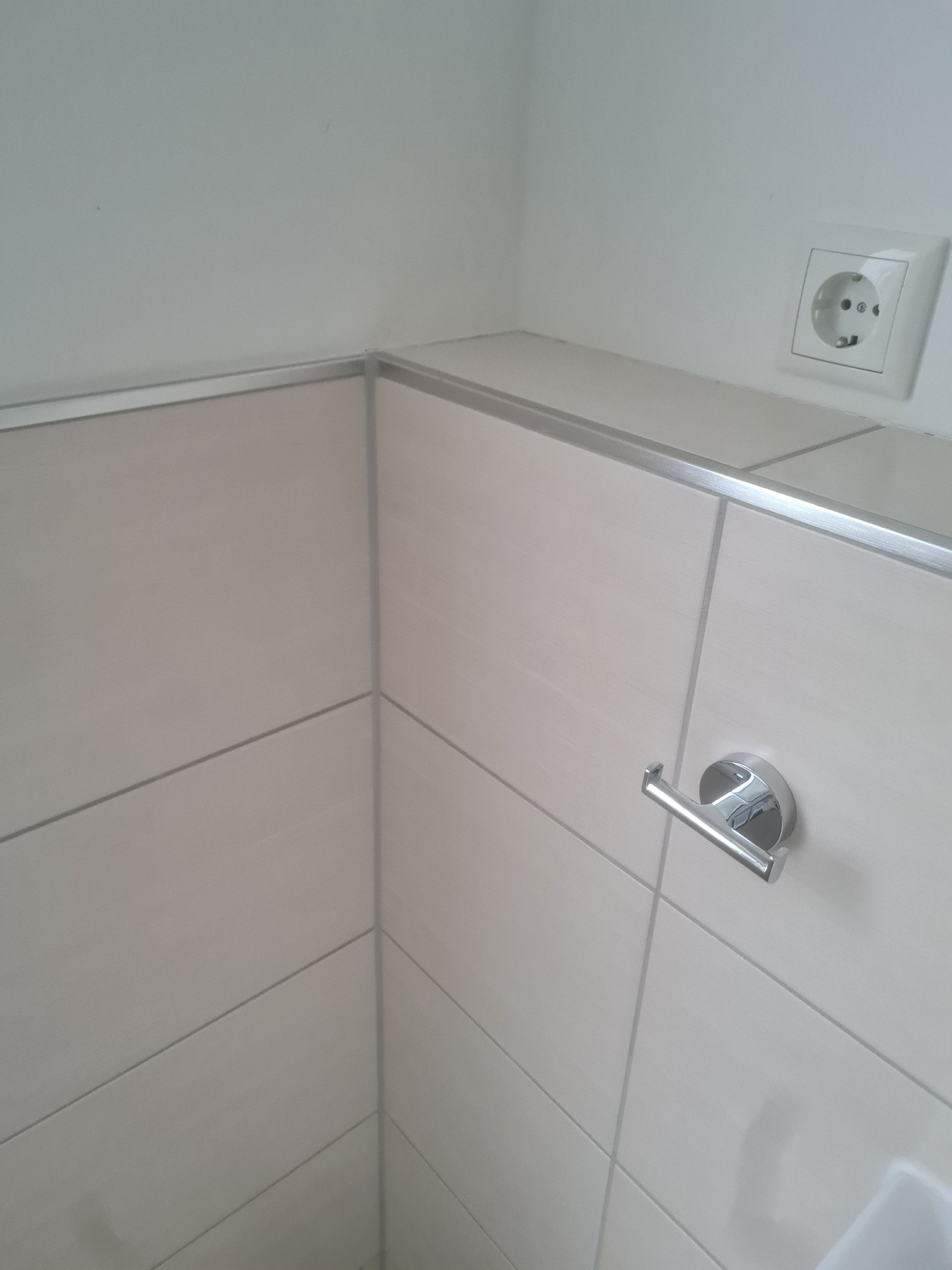 Jasne, poziome płytki w łazience z chromowanym uchwytem na ręcznik i gniazdkiem elektrycznym. Wykończenie listwą. Minimalistyczny design.