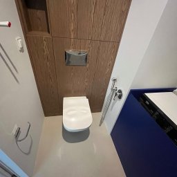 Babylon Mateusz Pytka - Nowoczesna toaleta podwieszana z drewnianą zabudową i bidetką w wykończonej łazience. Ujęcie z góry podkreśla minimalistyczny design i funkcjonalność.