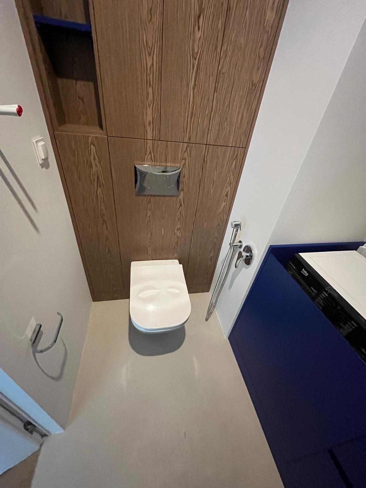 Nowoczesna toaleta podwieszana z drewnianą zabudową i bidetką w wykończonej łazience. Ujęcie z góry podkreśla minimalistyczny design i funkcjonalność.