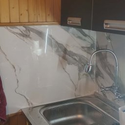 Kuchnia po remoncie: marmurowe płytki na ścianie nad zlewem, ciemne szafki wiszące, drewniane wykończenie, ręczniki na wieszaku. Widok na odnowione wnętrze.