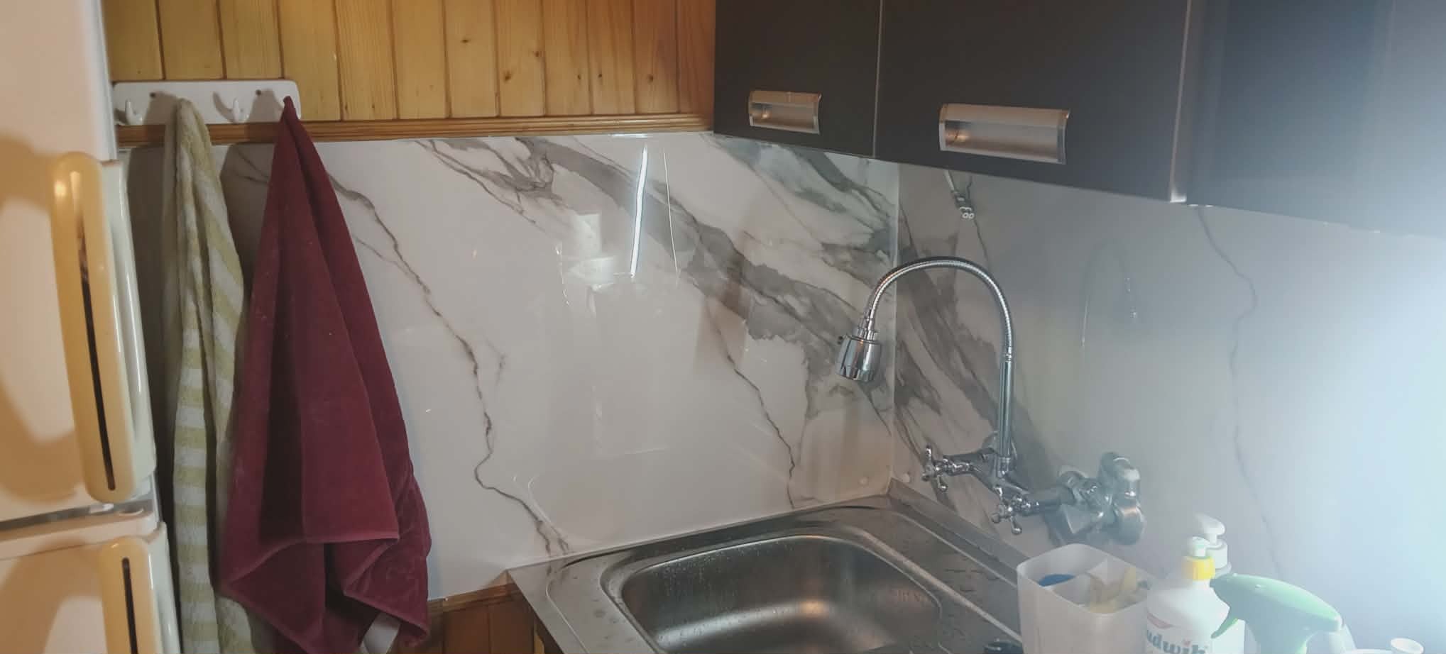 Kuchnia po remoncie: marmurowe płytki na ścianie nad zlewem, ciemne szafki wiszące, drewniane wykończenie, ręczniki na wieszaku. Widok na odnowione wnętrze.