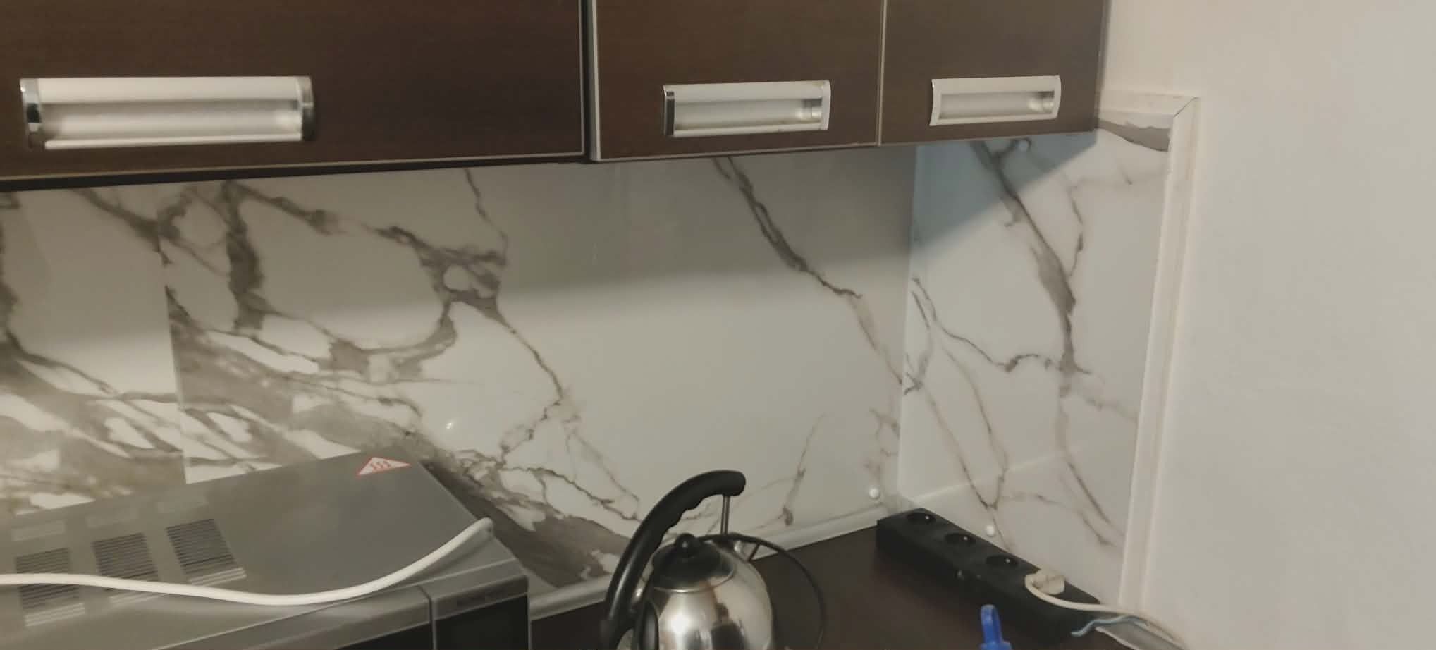 Kuchnia po remoncie: brązowe szafki wiszące nad blatem z marmurowym wzorem. Widoczny czajnik i gniazdko elektryczne. Ukończone wykończenie ściany.