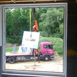 DOBRY MONTAŻ Mariusz Szpakowski - Montaż okna z użyciem dźwigu na budowie. Widok z wnętrza budynku przez otwór okienny na ciężarówkę z dźwigiem podnoszącym szybę okienną.