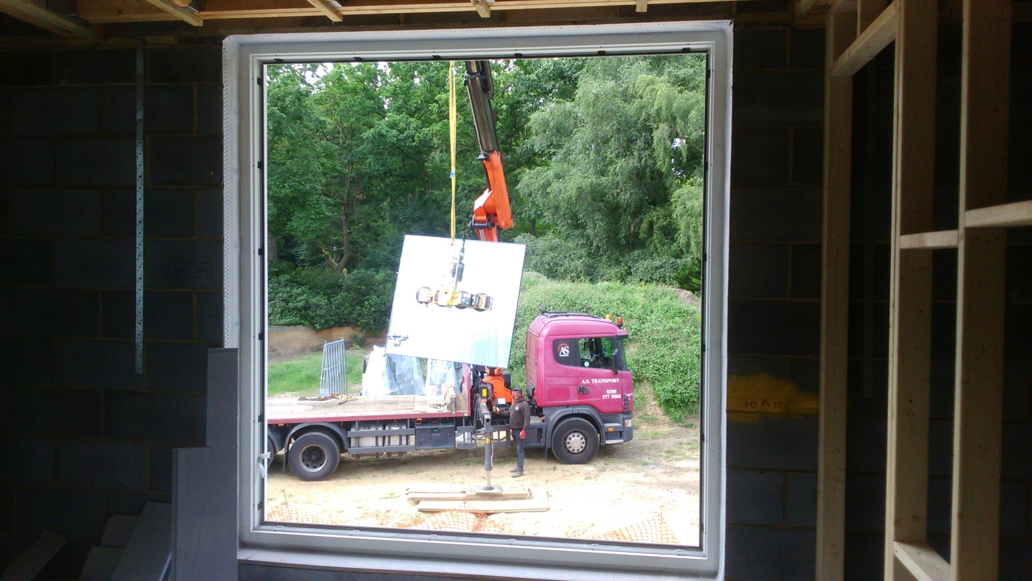 Montaż okna z użyciem dźwigu na budowie. Widok z wnętrza budynku przez otwór okienny na ciężarówkę z dźwigiem podnoszącym szybę okienną.