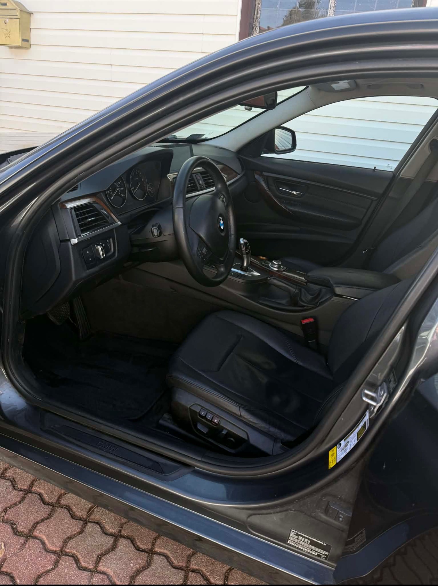 Wnętrze czarnego samochodu BMW z czarną skórzaną tapicerką, widok z otwartych drzwi kierowcy. Widoczna deska rozdzielcza i fotele.