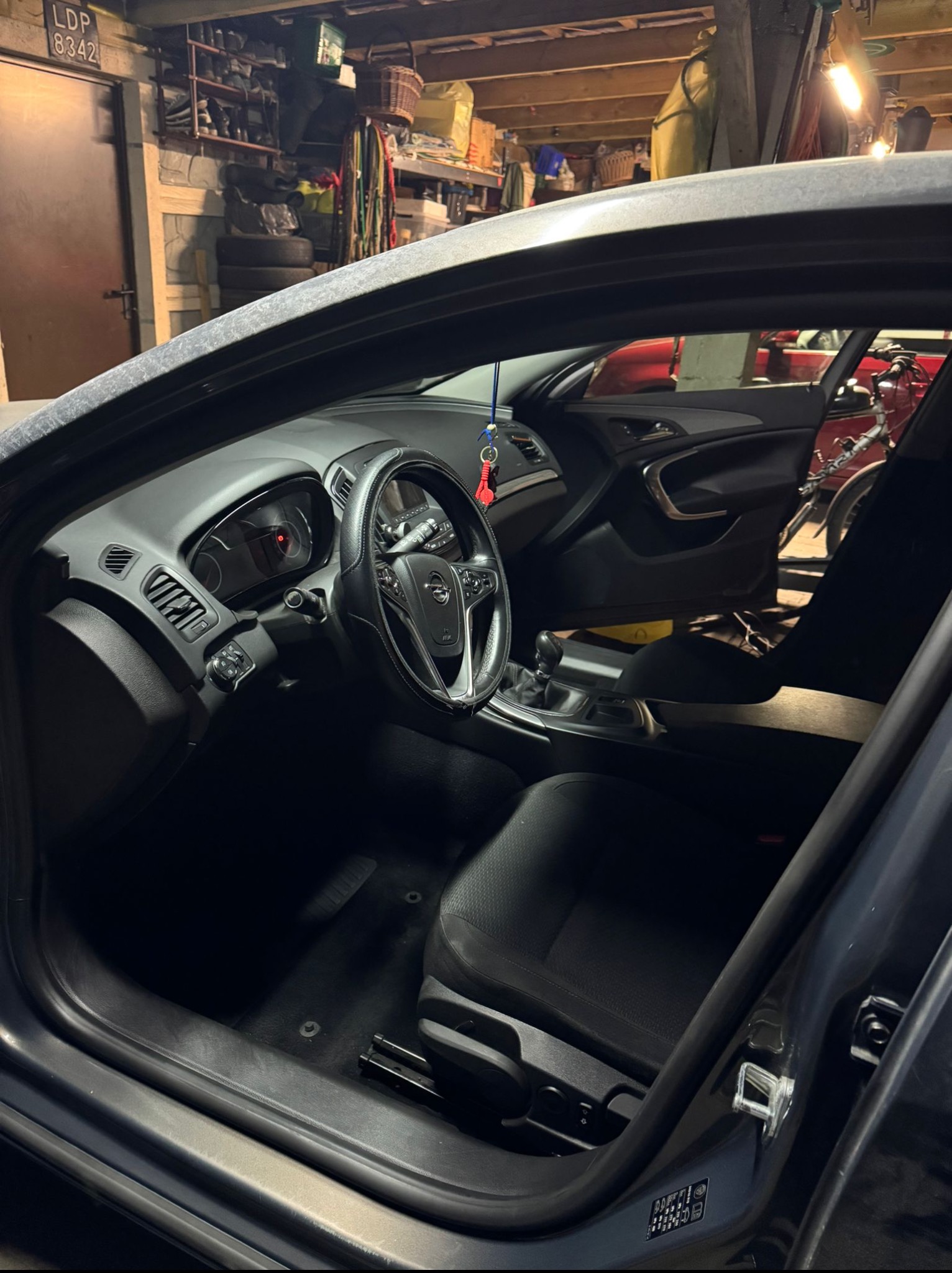 Wnętrze samochodu Opel Insignia z widocznymi czarnymi fotelami, deską rozdzielczą i kierownicą. W tle garaż z rowerem i regałami.