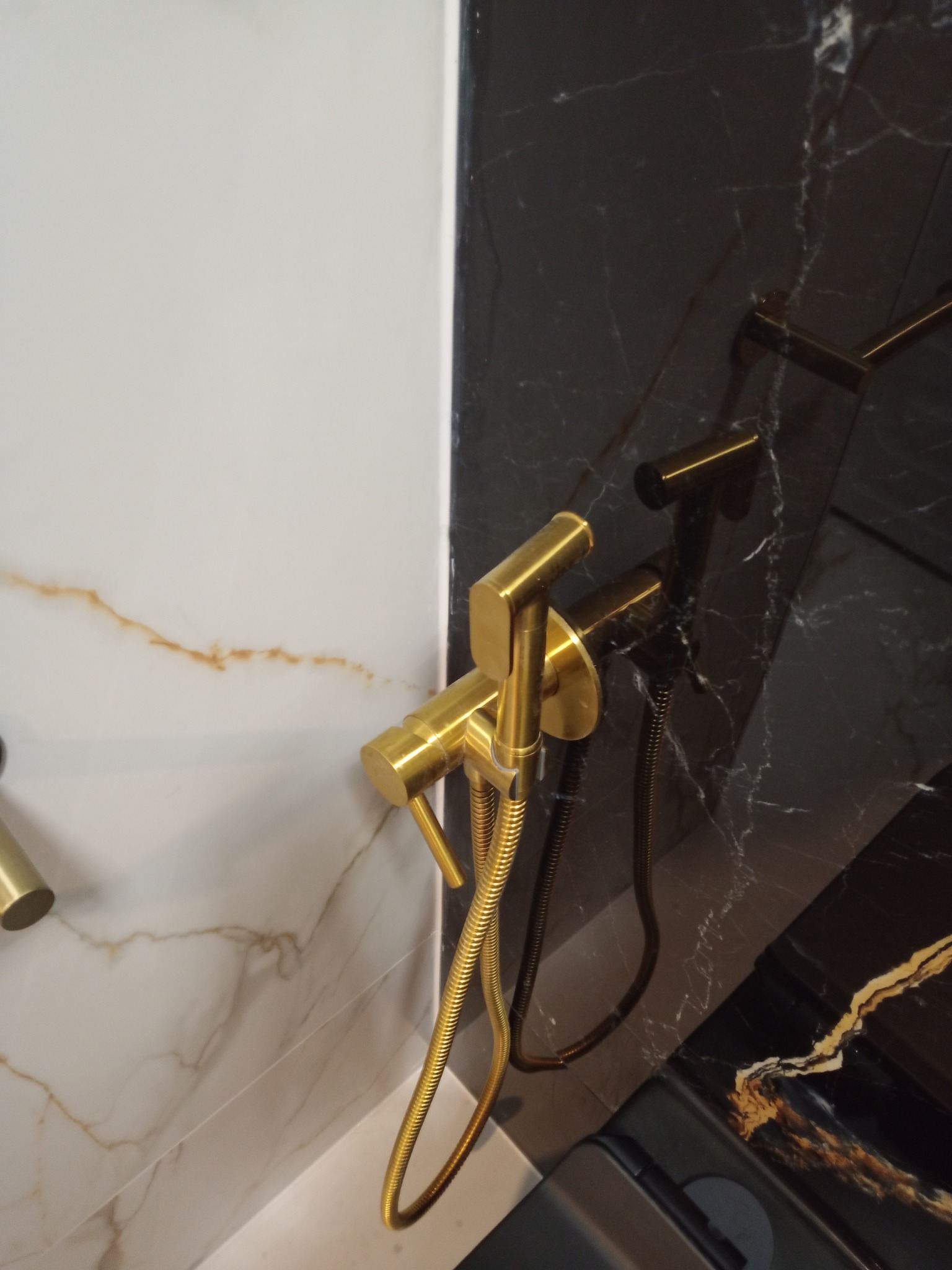 Złoty bidet natryskowy na tle marmurowych płytek w odcieniach bieli i czerni. Luksusowe wykończenie łazienki z dbałością o detale.