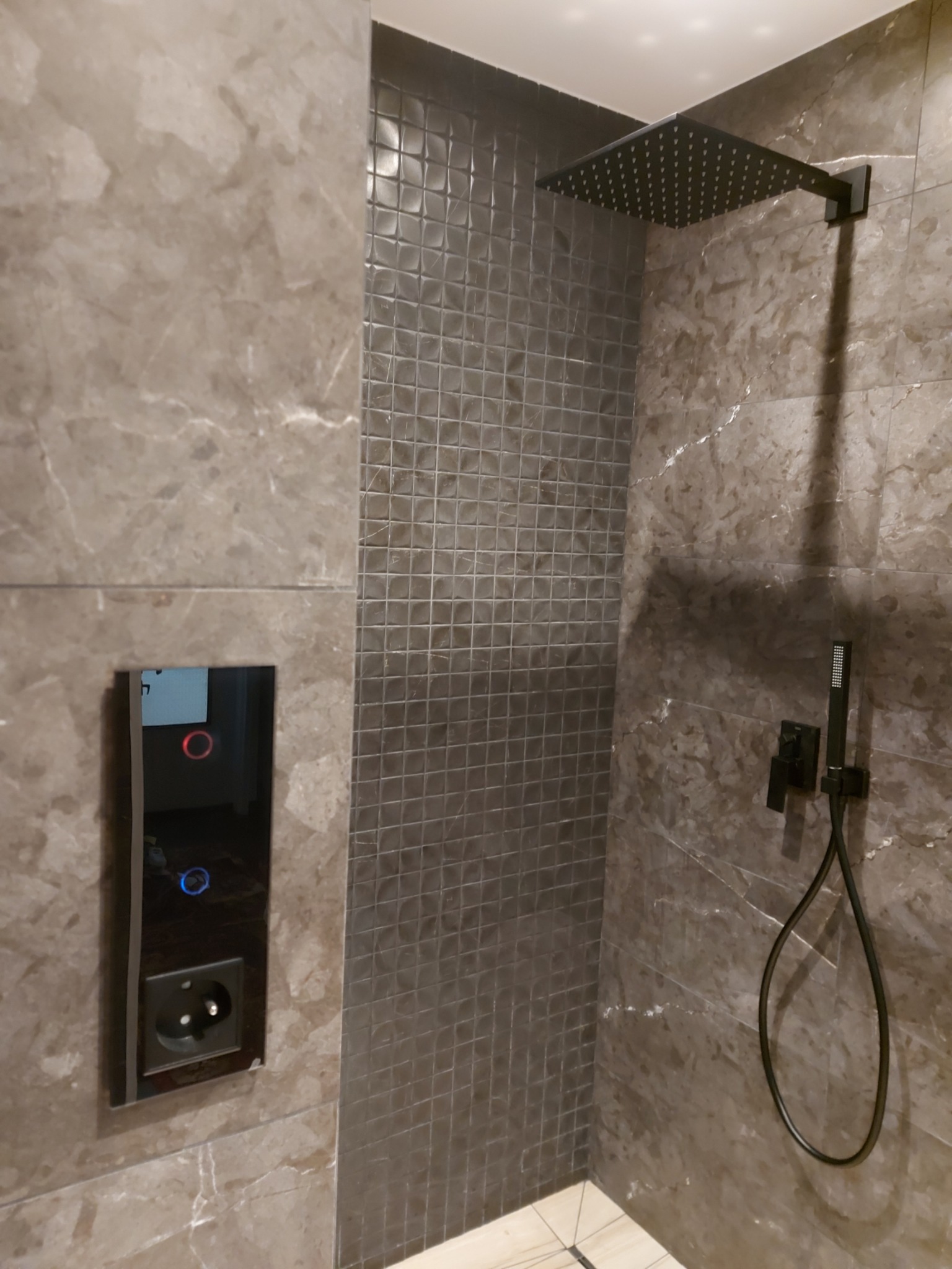 Nowoczesna kabina prysznicowa z marmurowymi płytkami, czarną armaturą i panelem sterowania dotykowego. Minimalistyczny design z akcentem na detale.