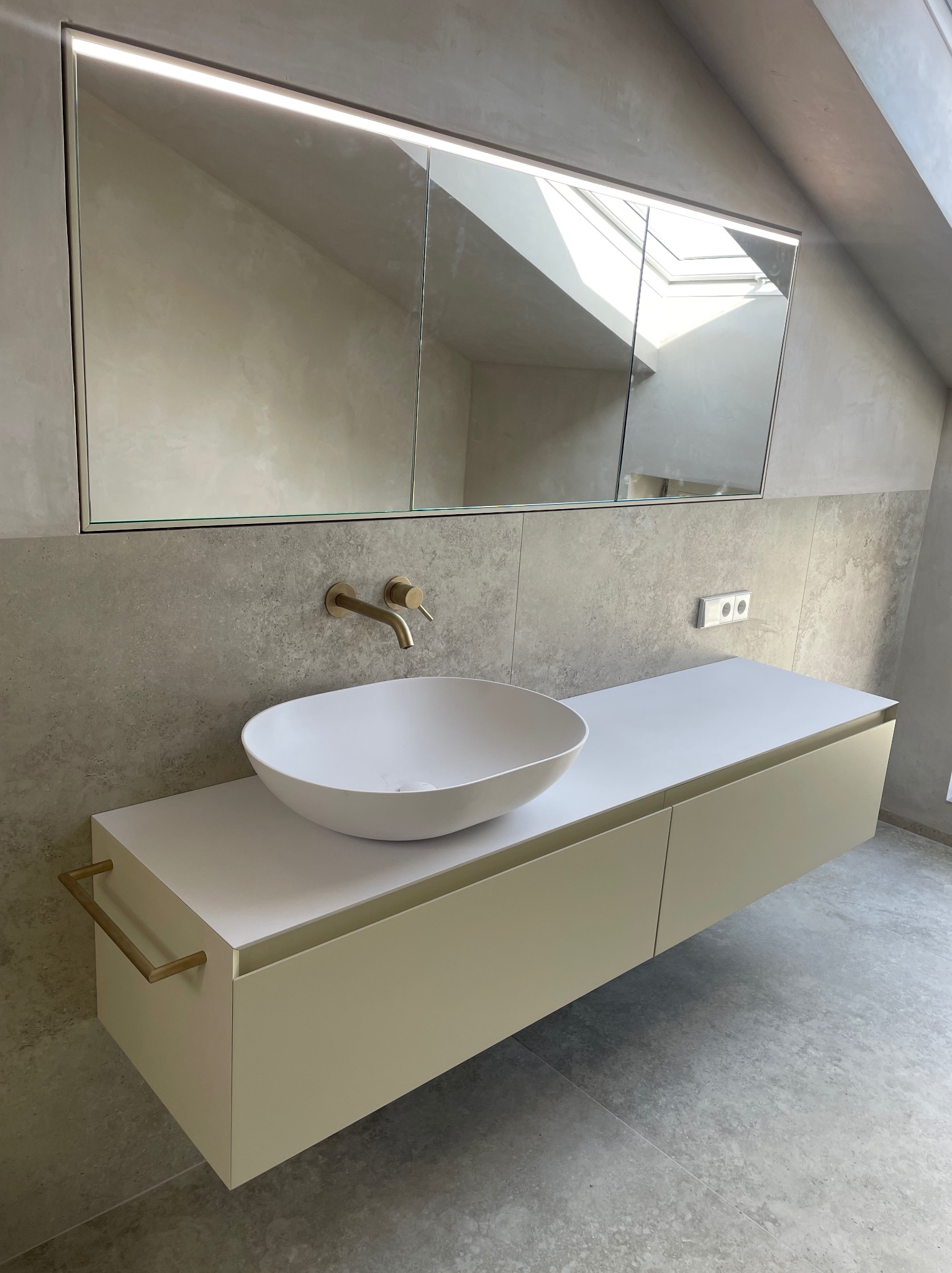 Nowoczesna łazienka na poddaszu: owalna umywalka, złota armatura, lustro z podświetleniem LED, szare płytki i skosy. Minimalistyczny design.