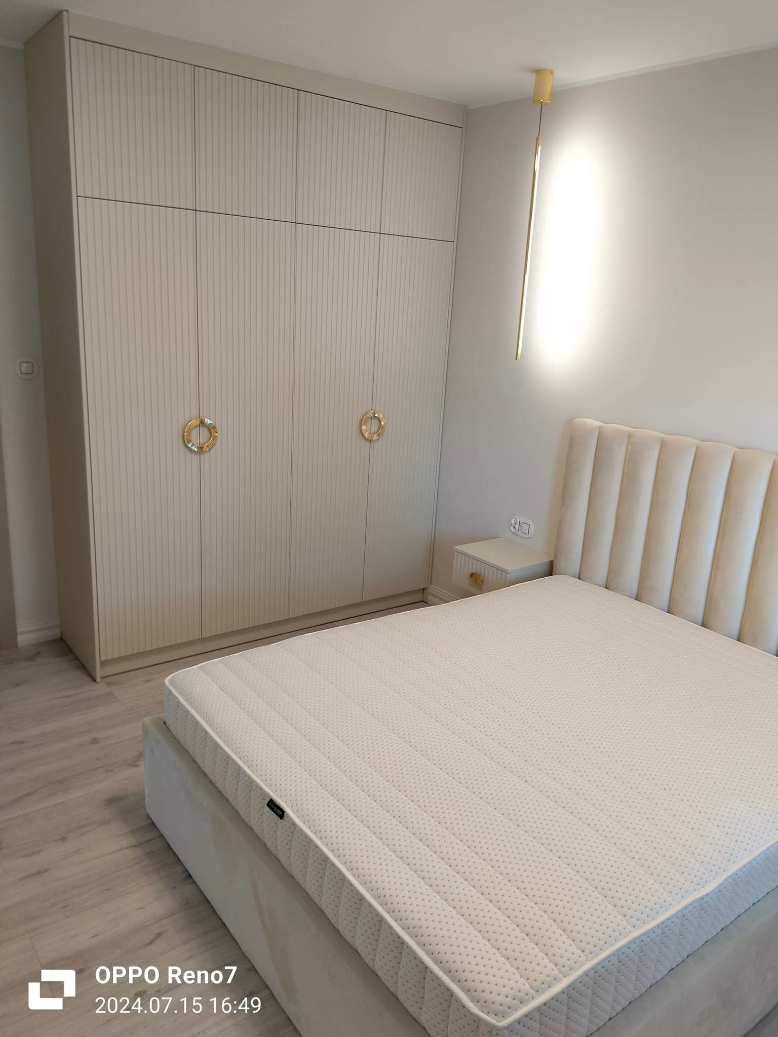 Jasna szafa wnękowa z ryflowanymi frontami i złotymi uchwytami w sypialni z łóżkiem i lampą. Minimalistyczny design, ciepłe oświetlenie.