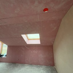 SZO-NE-BUD OLEH PYLYPCHUK - Pokój po montażu różowych płyt karton-gips na ścianach i suficie, widoczne okna dachowe i otwór na oświetlenie. Część ściany wyszpachlowana na gładko.