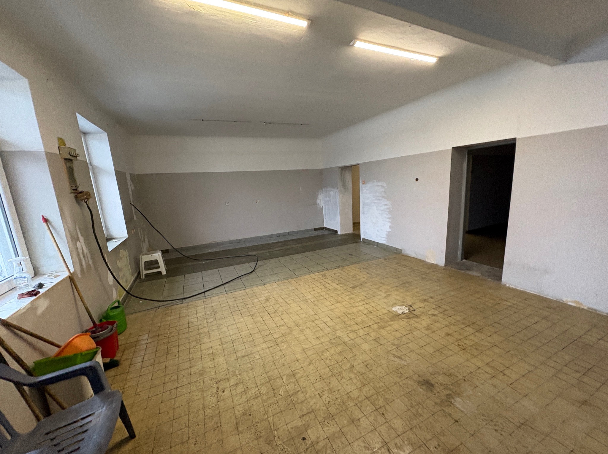 Wnętrze w trakcie remontu: widoczne przygotowane ściany do malowania, częściowo położona nowa podłoga, narzędzia malarskie przy oknie. Prace wykończeniowe w pomieszczeniu.