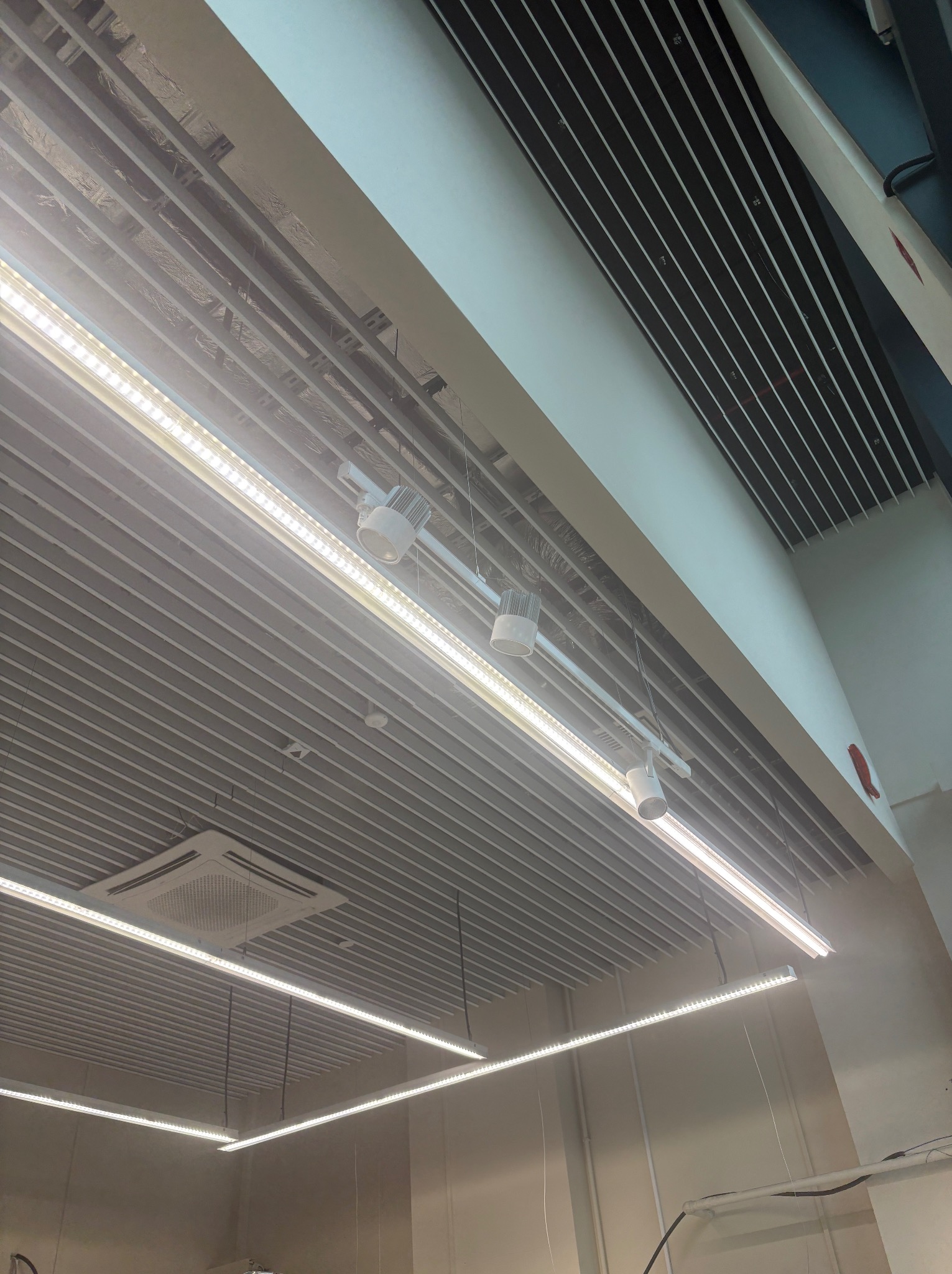 Nowoczesny sufit rastrowy z oświetleniem LED i reflektorami punktowymi w biurze. Widoczne elementy instalacji wentylacyjnej i klimatyzacji.