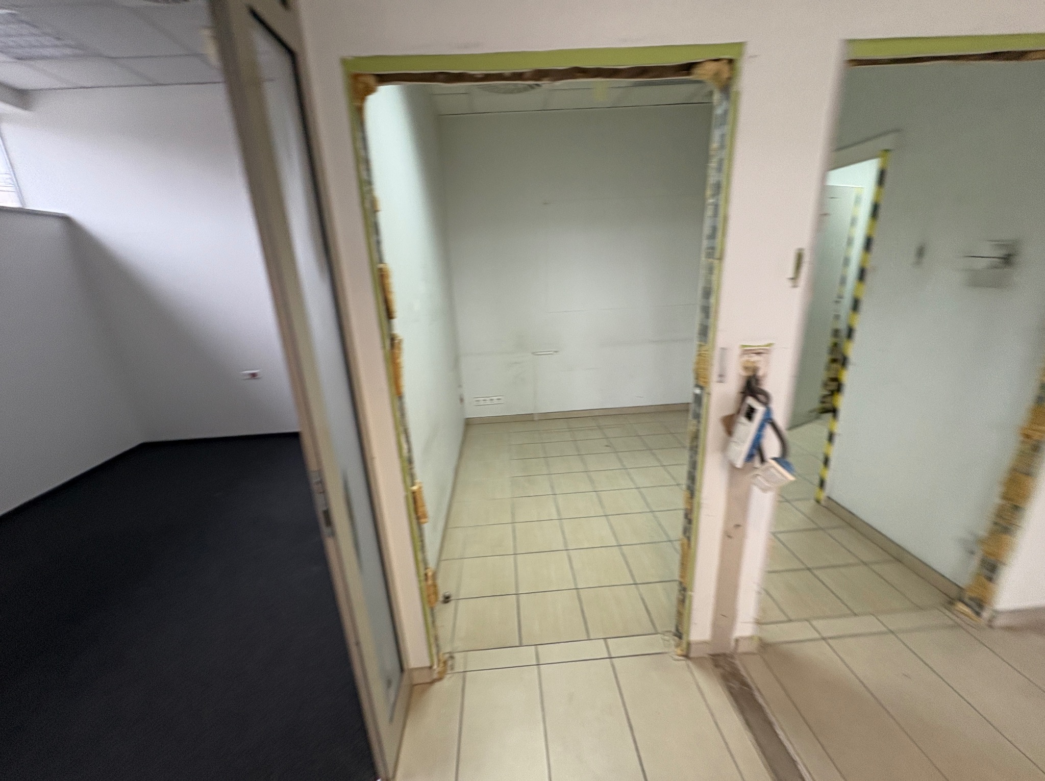 Wnętrze biura w trakcie remontu. Widoczne przygotowane ościeżnice drzwiowe, surowe ściany i podłoga z płytek. Perspektywa z korytarza.