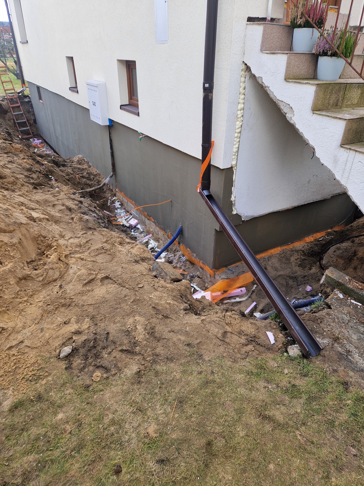 Ocieplenie fundamentów domu jednorodzinnego z widoczną izolacją termiczną i wykopem, przygotowane do dalszych prac ziemnych.