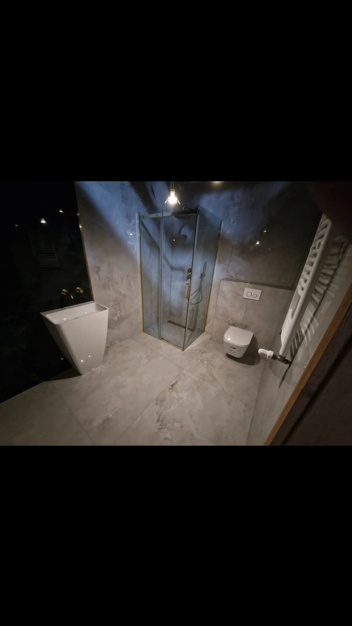 Nowoczesna łazienka z kabiną prysznicową, umywalką na blacie i grzejnikiem drabinkowym. Płytki imitujące marmur na podłodze i ścianach. Minimalistyczny design.