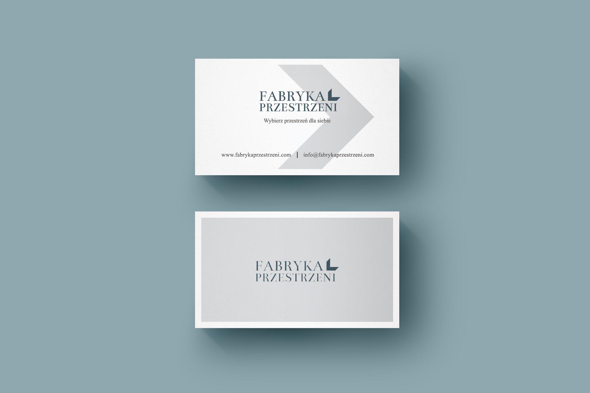 Dwie wizytówki firmy 'Fabryka Przestrzeni' na gładkim, błękitnym tle. Górna wizytówka zawiera adres strony internetowej i adres e-mail. Minimalistyczny design.