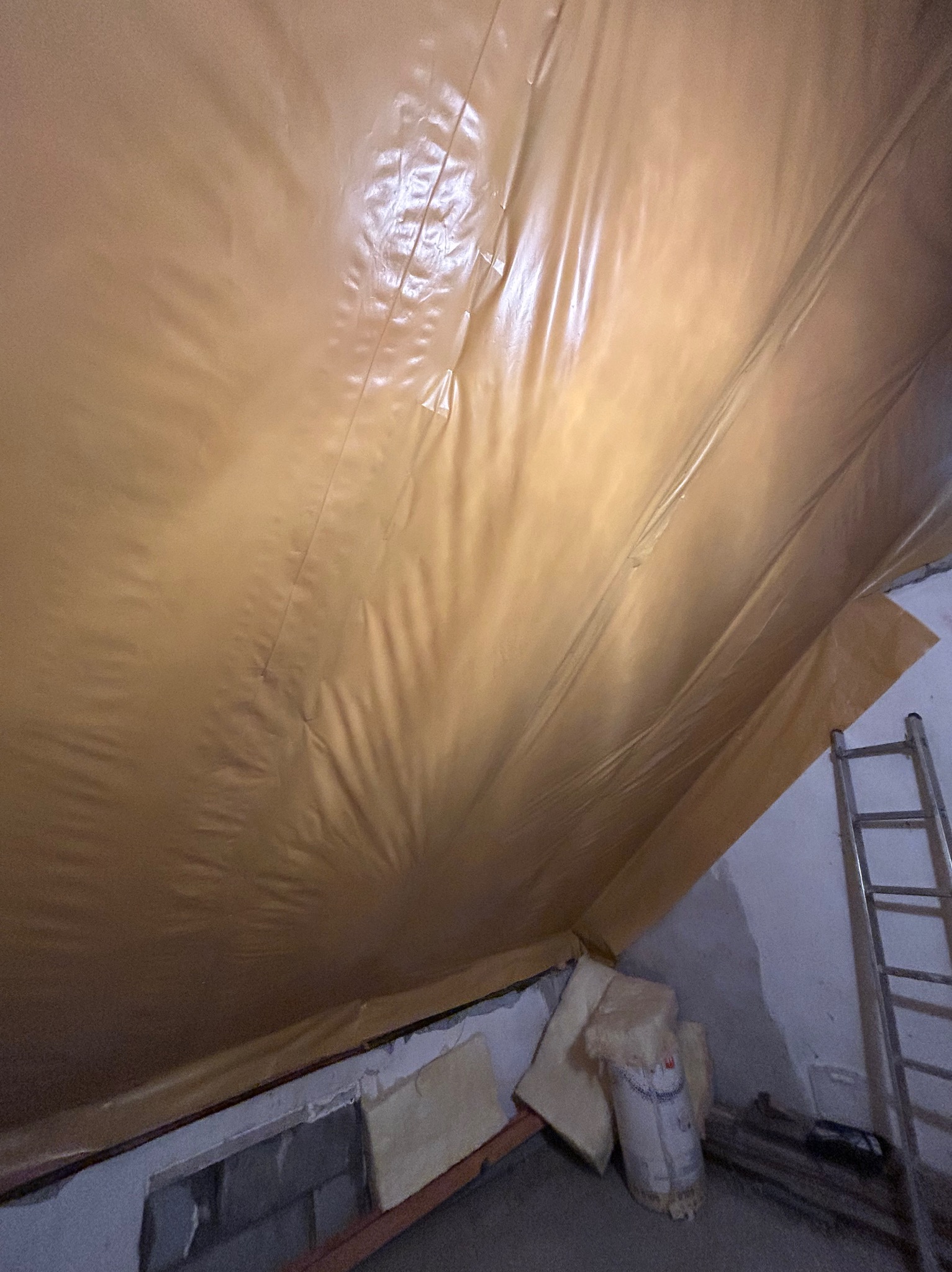 Poddasze w trakcie ocieplania: folia paroizolacyjna, wełna mineralna i drabina. Widok z dołu, ukazujący postęp prac.