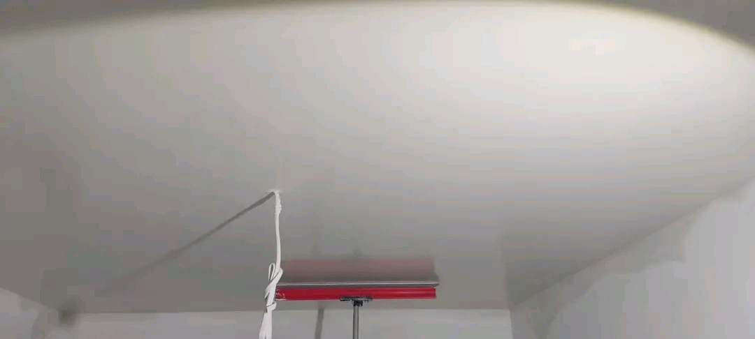 Biały sufit po szpachlowaniu, widoczny fragment narzędzia z czerwoną obudową i sznurkiem. Oświetlenie punktowe podkreśla gładką powierzchnię.