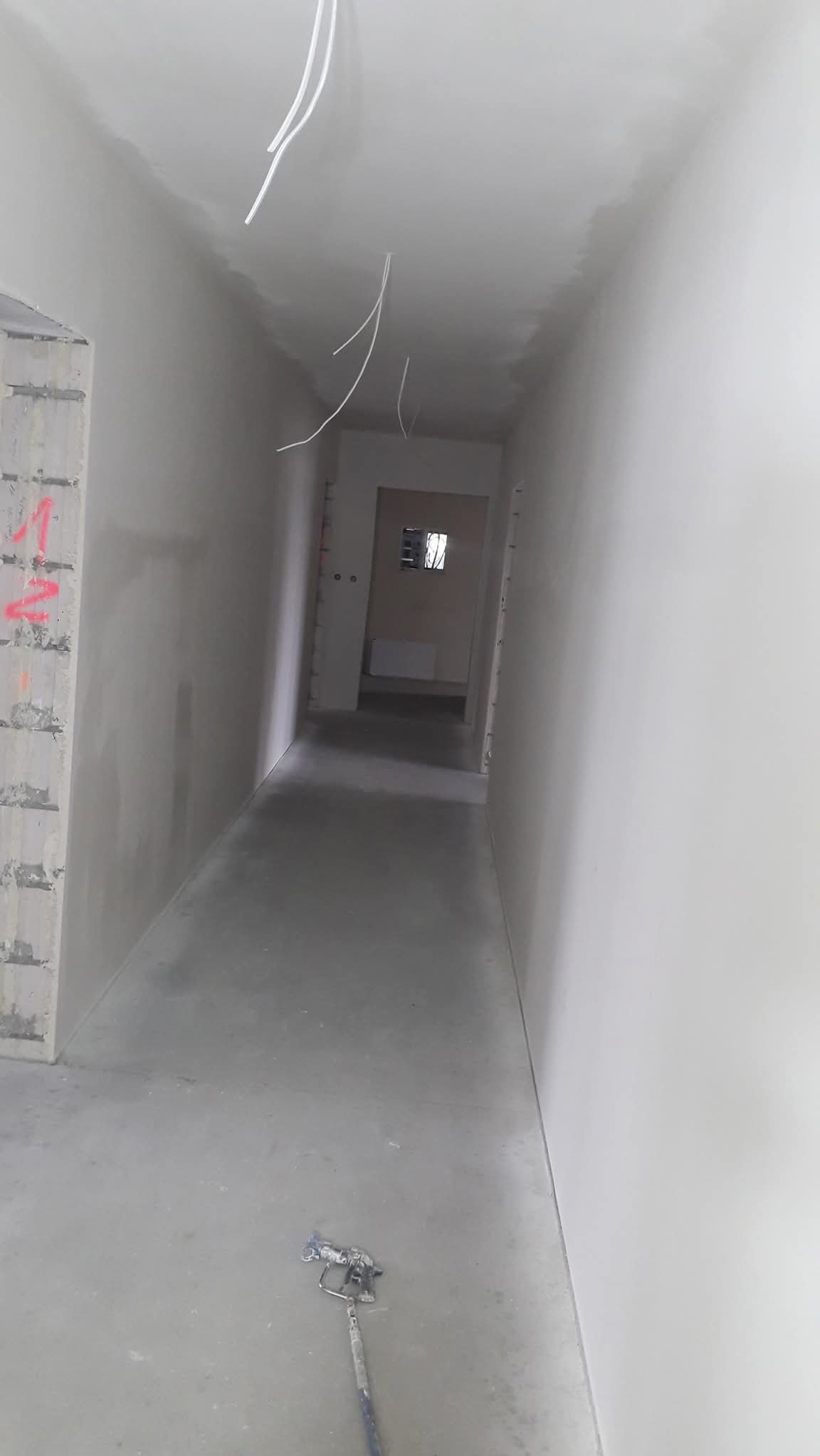 Korytarz po szpachlowaniu, widoczne gładkie ściany przygotowane do malowania. Na podłodze leży narzędzie do malowania natryskowego.