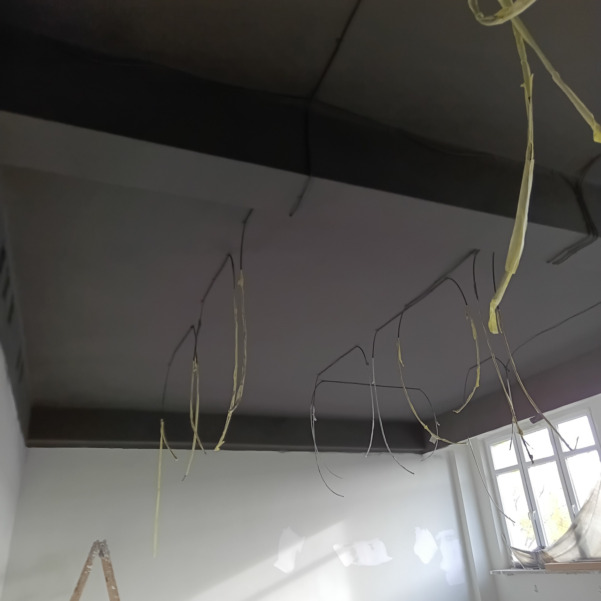 Szpachlowana sufitowa płyta gipsowa z widocznymi przewodami elektrycznymi zabezpieczonymi taśmą. W tle okno i fragment drabiny malarskiej.