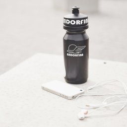 Karol Maryniak - Czarna butelka z logo Endorfina, biały smartfon i słuchawki na jasnym tle. Minimalistyczne ujęcie akcesoriów sportowych.