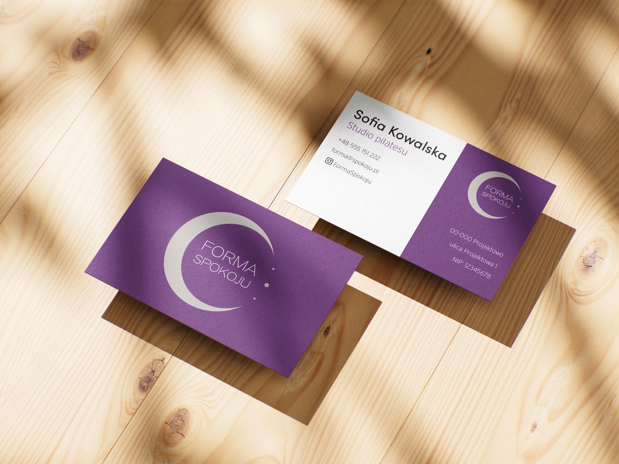 Dwie wizytówki w odcieniach fioletu i bieli z logo 'Forma Spokoju' leżą na drewnianym stole w ciepłym świetle. Minimalistyczny design, czcionka bezszeryfowa.