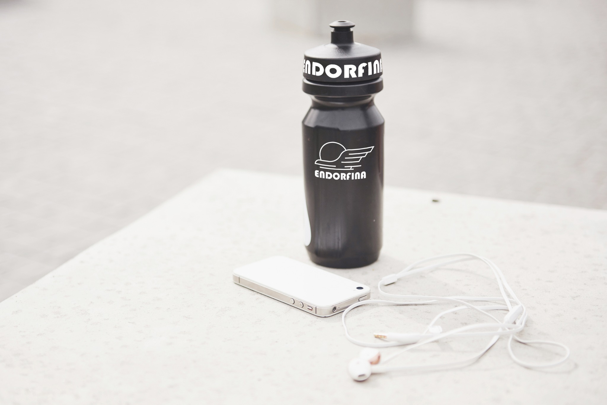 Czarna butelka z logo Endorfina, biały smartfon i słuchawki na jasnym tle. Minimalistyczne ujęcie akcesoriów sportowych.