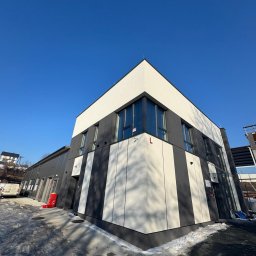 HKTEAM - Nowoczesny budynek biurowy z elewacją w biało-szare pasy, widziany z dołu pod kątem, z fragmentem oblodzonego chodnika i błękitnym niebem w tle.