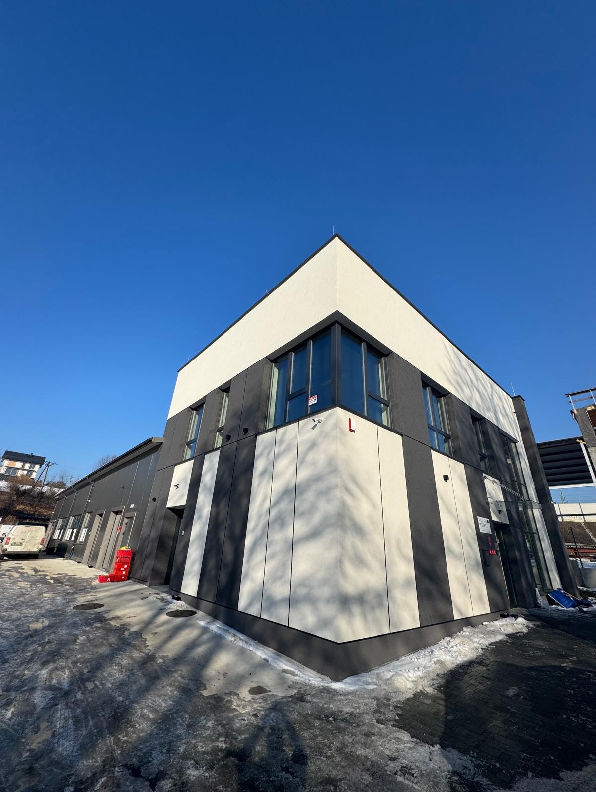 Nowoczesny budynek biurowy z elewacją w biało-szare pasy, widziany z dołu pod kątem, z fragmentem oblodzonego chodnika i błękitnym niebem w tle.