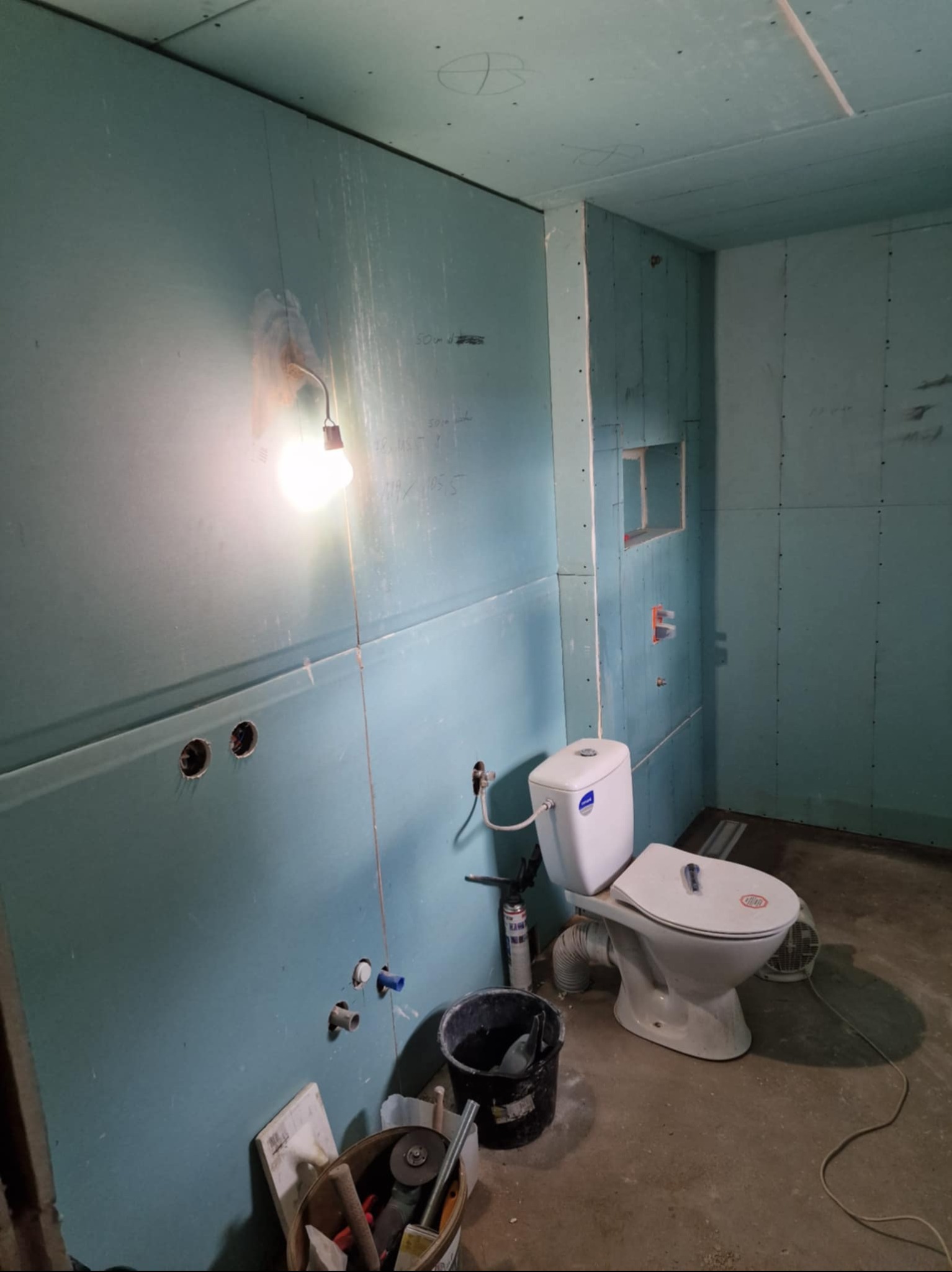 Łazienka w trakcie remontu w Grodzisku Wielkopolskim: ściany z płyt karton-gips, zamontowana toaleta, widoczne instalacje i narzędzia. Oświetlenie robocze.