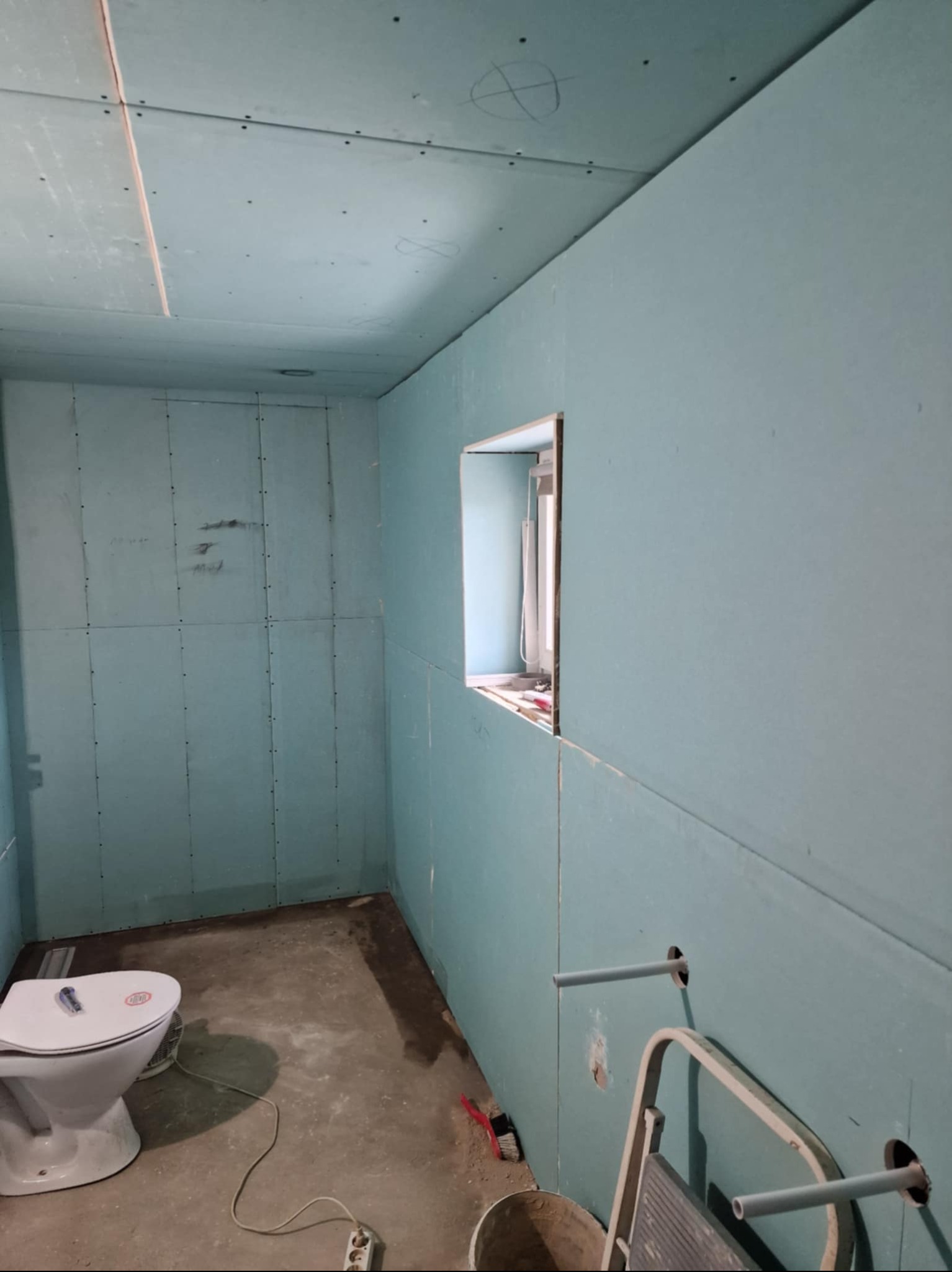 Łazienka w trakcie montażu płyt kartonowo-gipsowych na ścianach i suficie, widoczne przygotowane otwory na instalacje i częściowo zamontowana toaleta.