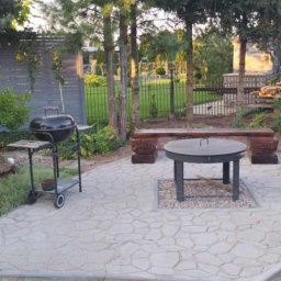 Przemysław Helpa - Ukończony taras z kamienną nawierzchnią, drewnianymi ławkami i grillem. Elementy małej architektury w ogrodzie, zieleń w tle.