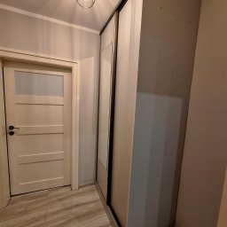 Przemysław Helpa - Wnętrze: zabudowa szafy przesuwnej z lustrem w przedpokoju, widoczna drewniana podłoga i drzwi. Oświetlenie sufitowe w stylu industrialnym.