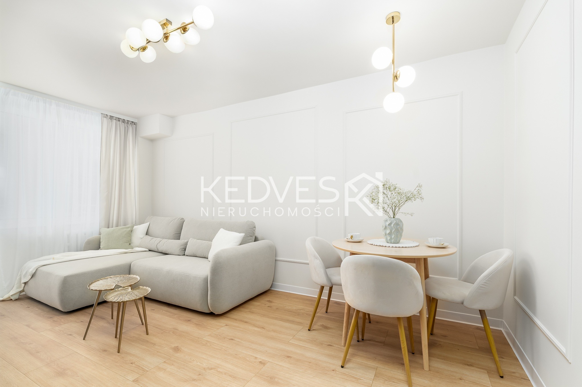 Jasne wnętrze: sofa z stolikami kawowymi, okrągły stół z krzesłami, drewniana podłoga, białe ściany z dekoracyjnymi listwami, nowoczesne lampy. Minimalistyczny design.