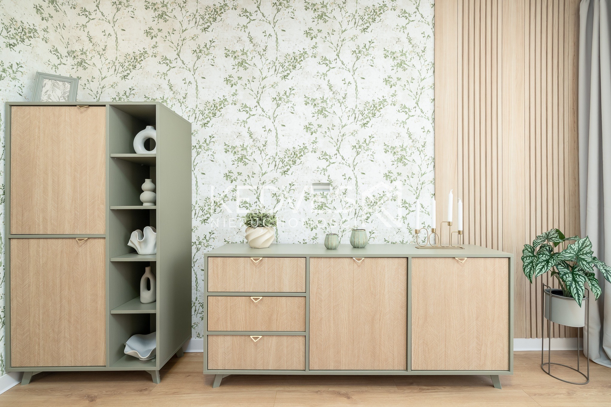 Stylowa aranżacja wnętrza: komoda z szufladami i szafka w odcieniach zieleni i drewna, dekoracje, tapeta w roślinny wzór, drewniana ściana z lamelami i roślina doniczkowa.