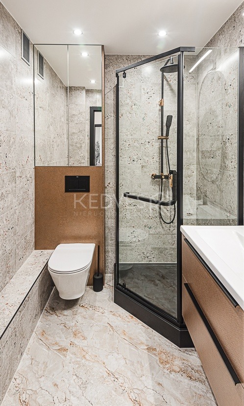 Nowoczesna łazienka z kabiną prysznicową typu walk-in, toaletą podwieszaną i marmurową podłogą. Uwagę zwraca czarna armatura i minimalistyczny design.