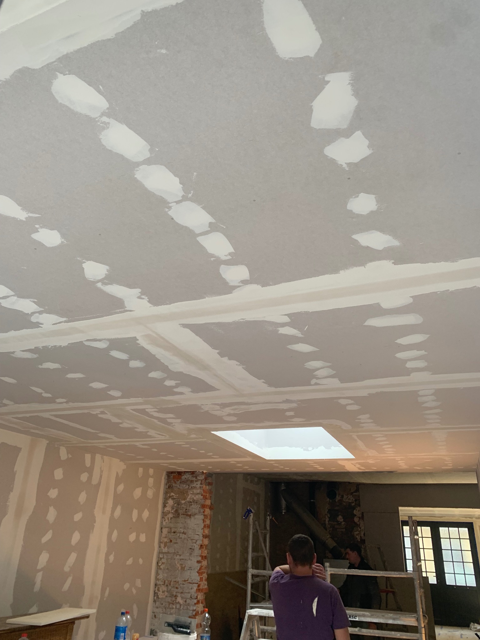 Sufit z płyt kartonowo-gipsowych, z widocznymi łączeniami i szpachlowanymi miejscami po wkrętach, przygotowany do malowania. W tle fragment ściany z odsłoniętą cegłą.