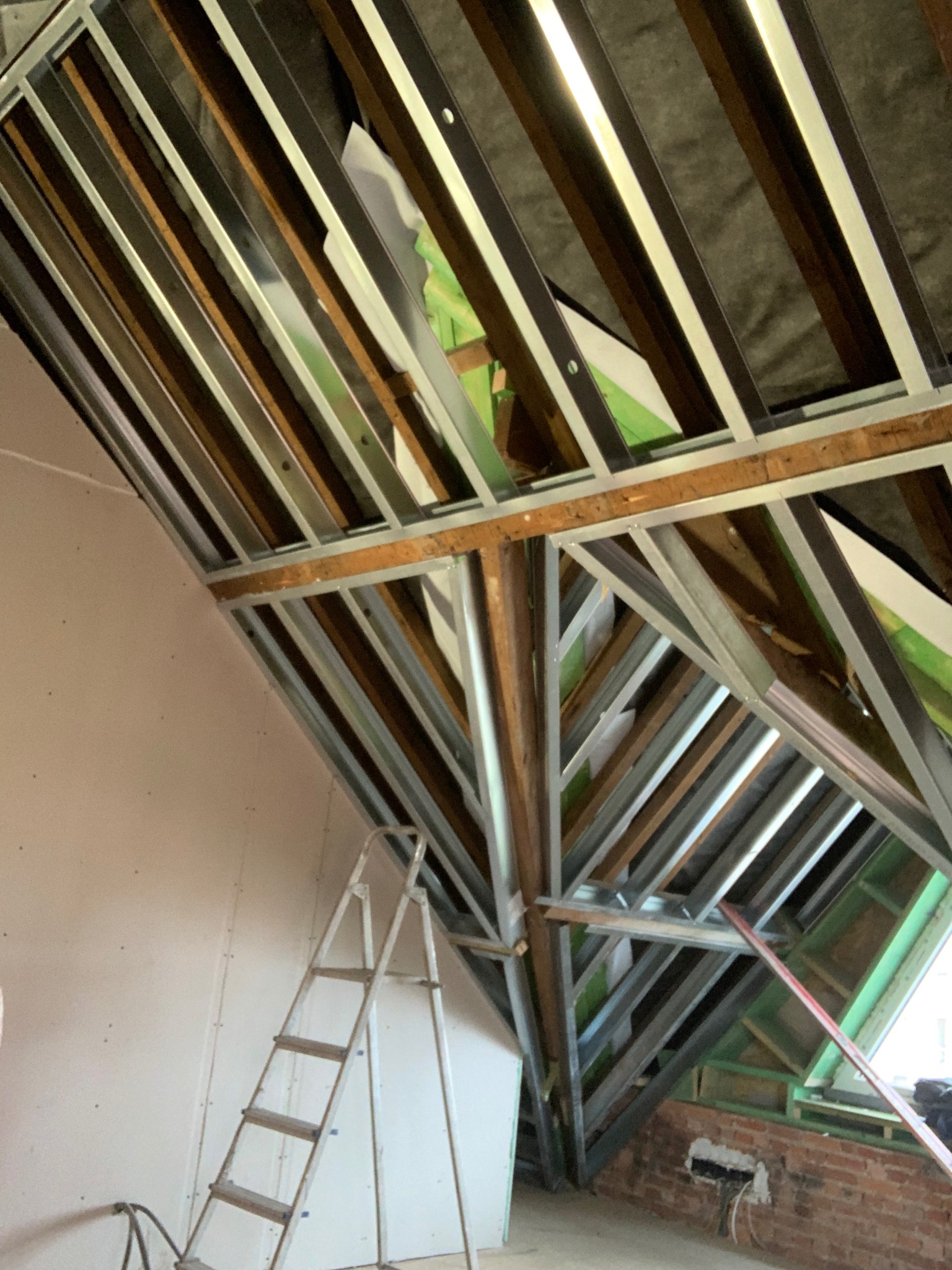 Skeletowa konstrukcja sufitu podwieszanego z profili metalowych i drewnianych łat, widoczna drabina, ściana z płyt gipsowo-kartonowych w trakcie montażu.