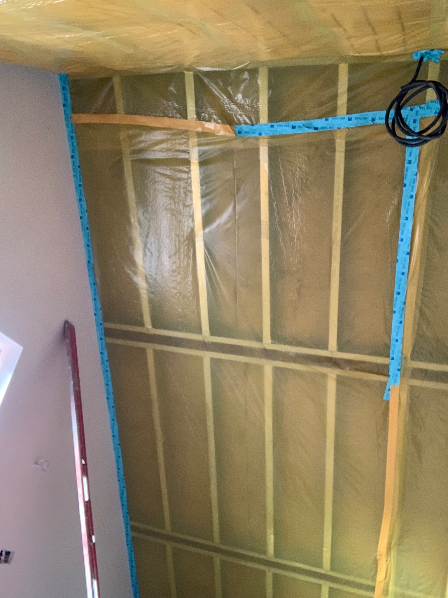 Szkielet sufitu podwieszanego z izolacją, zabezpieczony folią i taśmą. Widoczny fragment ściany z poziomnicą. Kabel elektryczny zwinięty w pętlę.