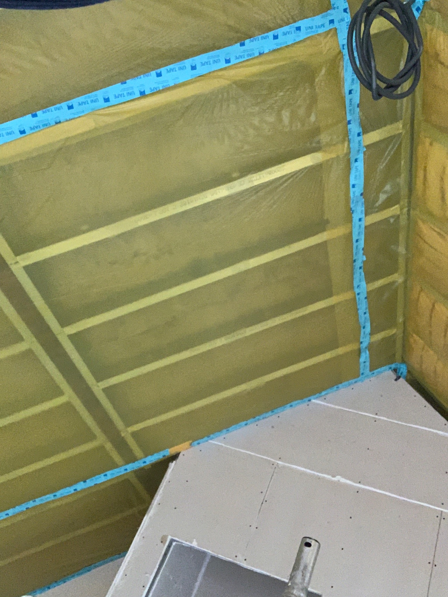 Montaż izolacji i płyt karton-gips na poddaszu. Widoczne drewniane belki, folia izolacyjna zabezpieczona niebieską taśmą, oraz fragment płyty gipsowej. Prace wykończeniowe.