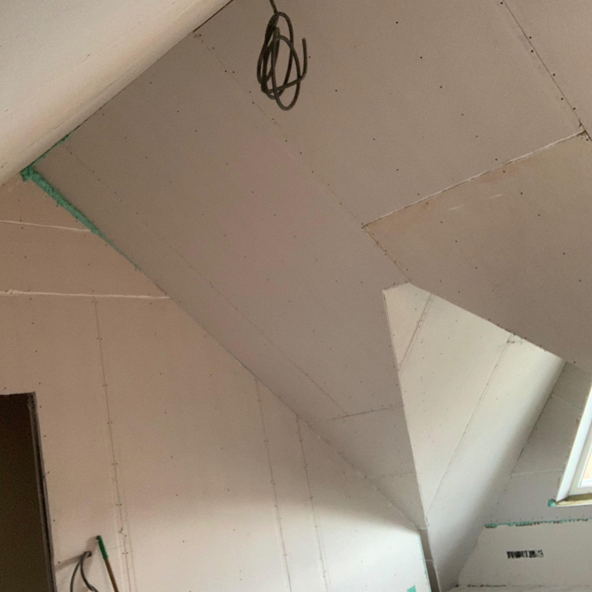 Poddasze z zamontowanymi płytami kartonowo-gipsowymi, widoczne łączenia płyt wypełnione pianką montażową, przewody elektryczne zwisające z sufitu.