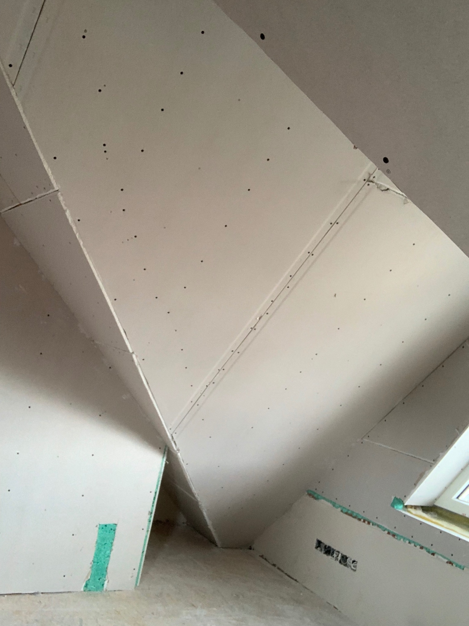 Skośny sufit poddasza wykończony płytami kartonowo-gipsowymi, widoczne łączenia i otwory po wkrętach, przygotowany do szpachlowania. Fragment okna dachowego.