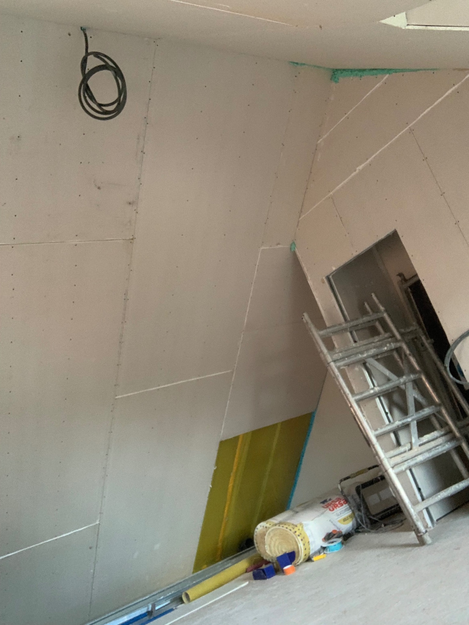 Skośna ściana z płyt karton-gips, częściowo ocieplona, z widoczną instalacją elektryczną i drabiną opartą o ścianę. Prace wykończeniowe w trakcie.