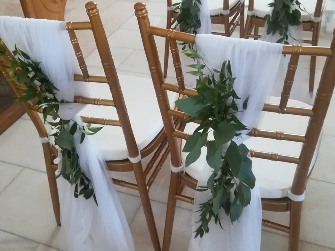 Dekoracje krzeseł z białym tiulem i zielonymi gałązkami, przygotowane na uroczystość w Janowie Lubelskim.