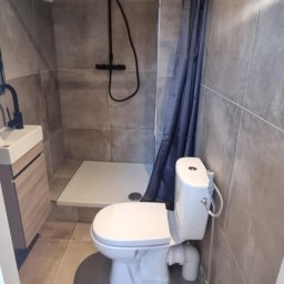 KAMIL SULOWSKI - Nowoczesna łazienka w szarościach: kabina prysznicowa typu walk-in, podwieszana toaleta z bidetką i umywalka z szafką. Uwagę zwraca czarna armatura i oświetlenie.