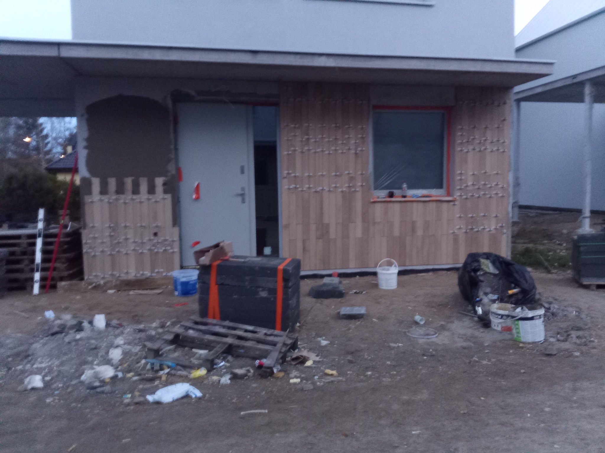 Montaż drewnopodobnej okładziny elewacyjnej na budynku jednorodzinnym. Widoczne narzędzia i materiały budowlane. Prace w toku, elewacja częściowo wykończona.