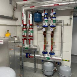 Kaskada pomp ciepła w kotłowni po modernizacji. Sześć pomp ciepła podłączonych do kotła olejowego. Rury z izolacją, manometry, zbiorniki wyrównawcze.