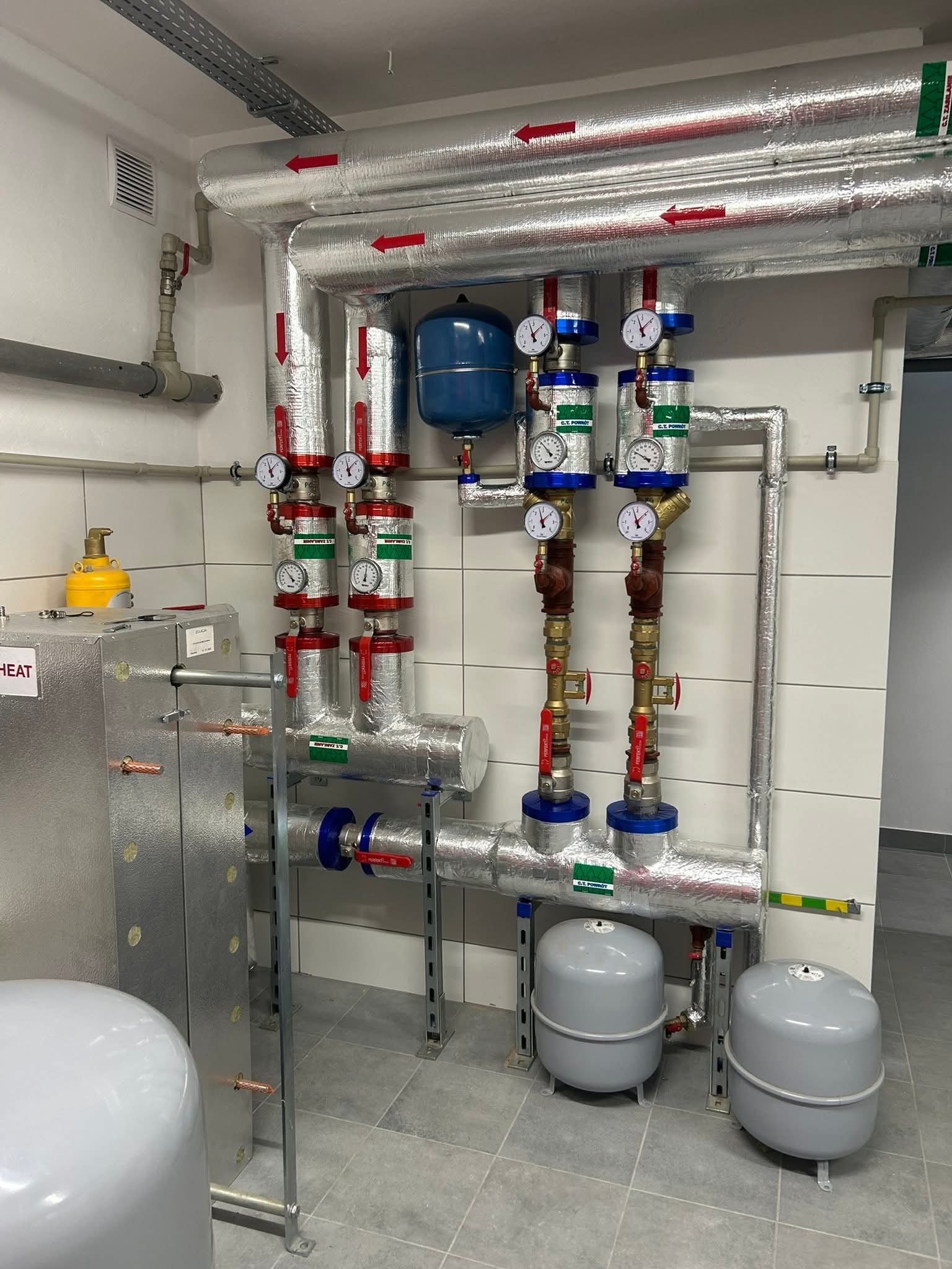 Kaskada pomp ciepła w kotłowni po modernizacji. Sześć pomp ciepła podłączonych do kotła olejowego. Rury z izolacją, manometry, zbiorniki wyrównawcze.